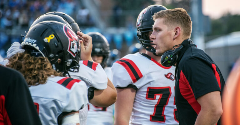 young football coach talking to players on the sideline during a game