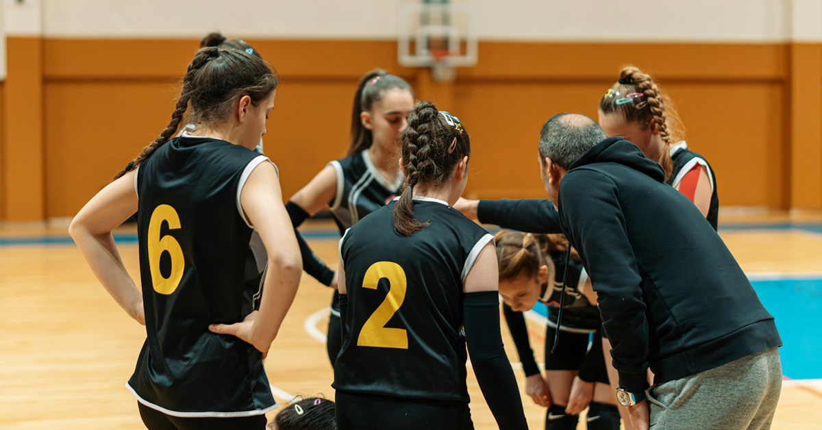 Coach giving instructions to female volleyball team in a huddle